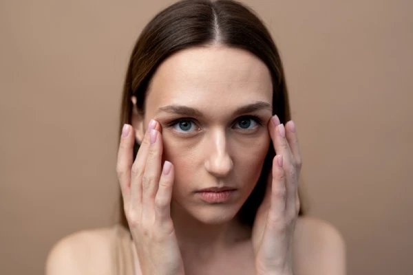 Femme examinant son contour des yeux pour des cernes creux devant un fond neutre.
